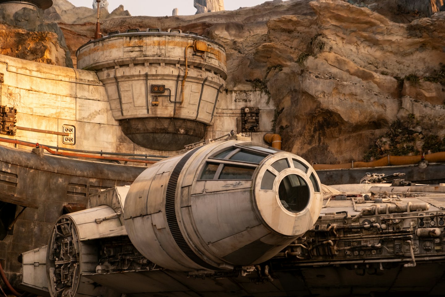 A weathered spaceship parked near an industrial structure on a desert planet.